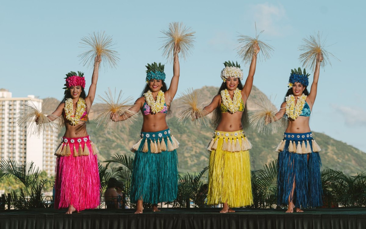 Hula dancers performing on the lawn at Aha Aina, with Diamond Head and the Waikiki skyline behind the stage