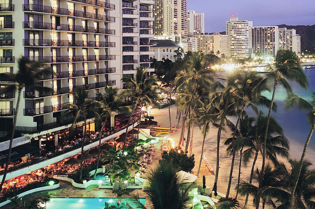 Duke's Waikiki lit up on the beachfront at dusk, with palms and Waikiki Beach