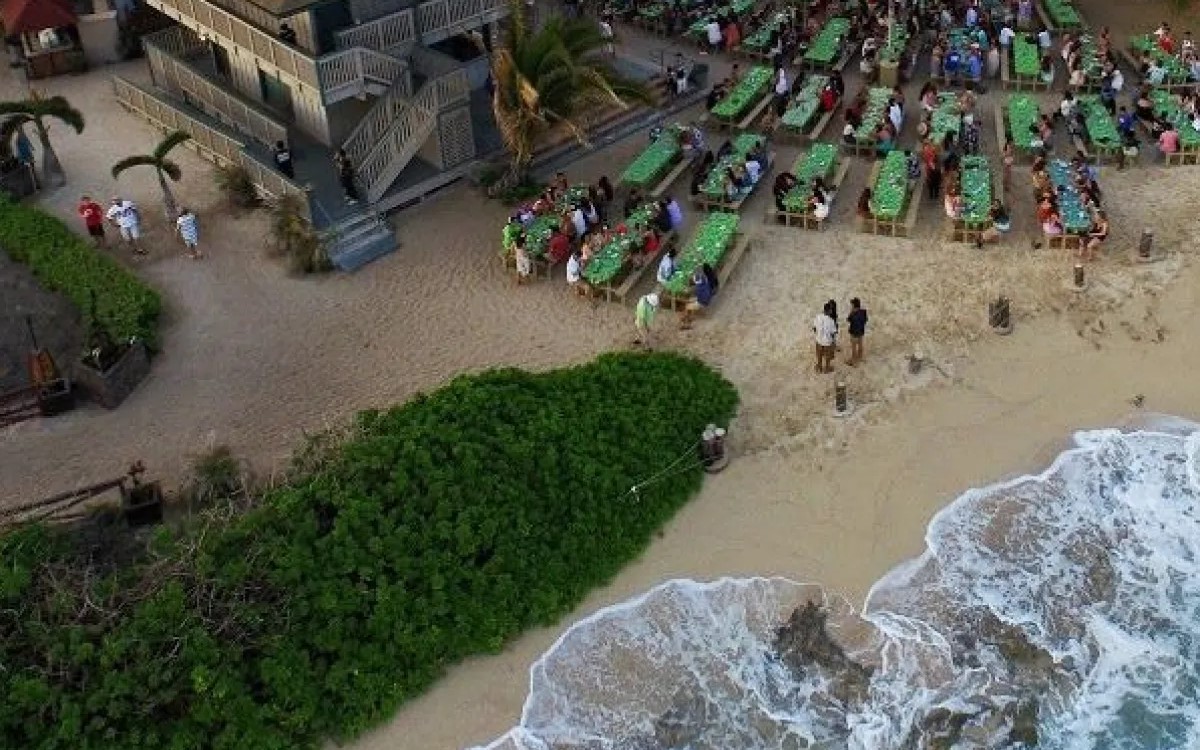Long tables set out on the sand at Germaines Luau, with the surf breaking at the edge of the dining area