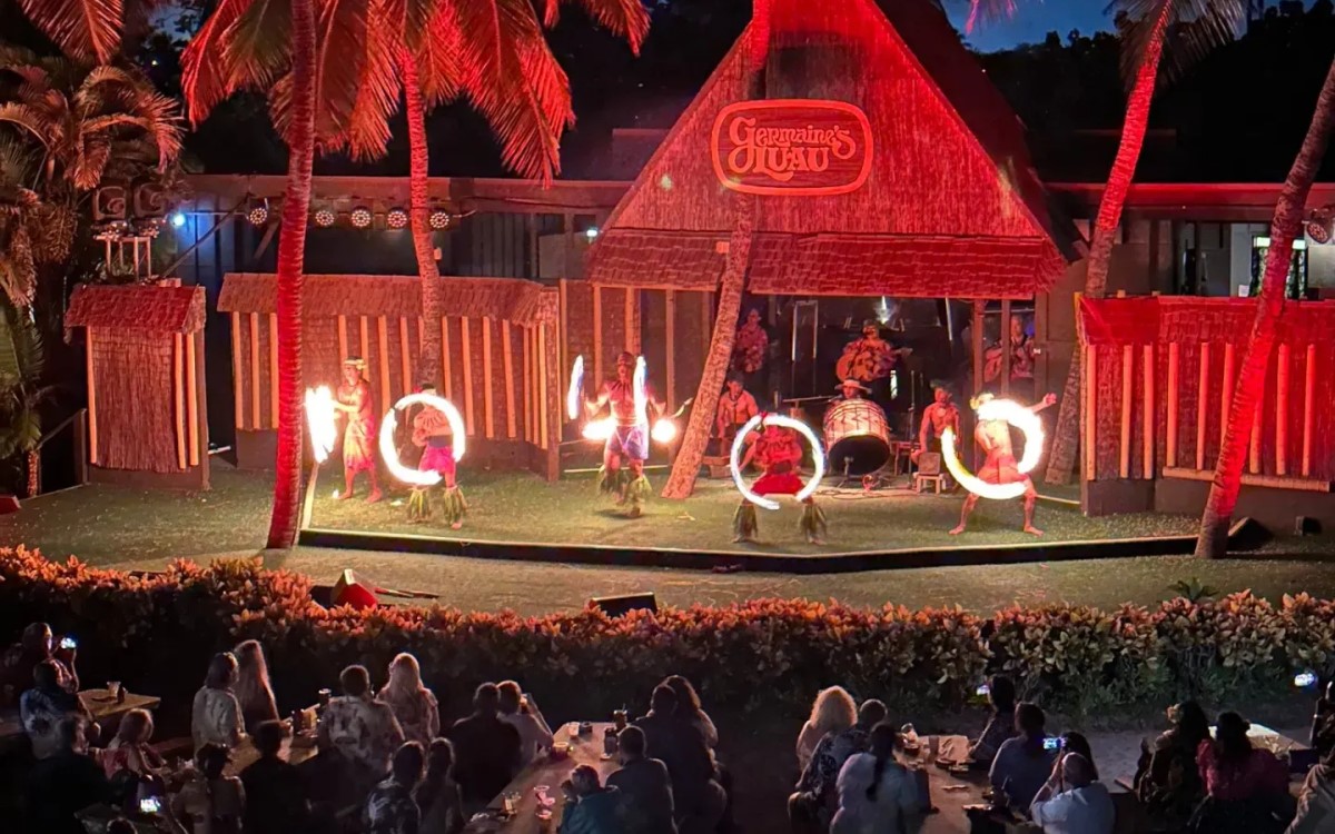Fire knife dancers on the thatched Germaines Luau stage lit red at night, with the audience seated in front